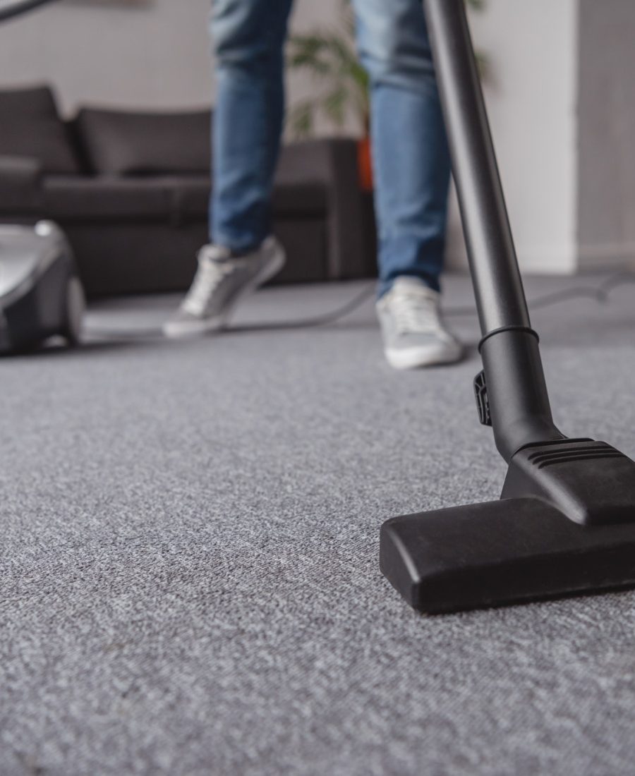 cropped image of man cleaning carpet in living room with vacuum cleaner
